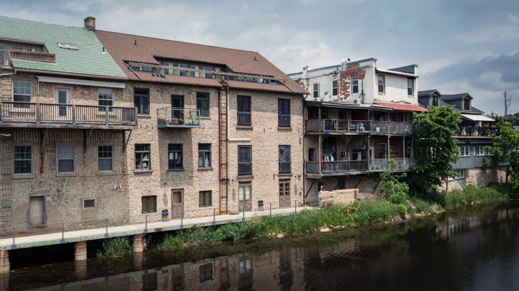 Old brick buildings line a calm river under cloudy skies