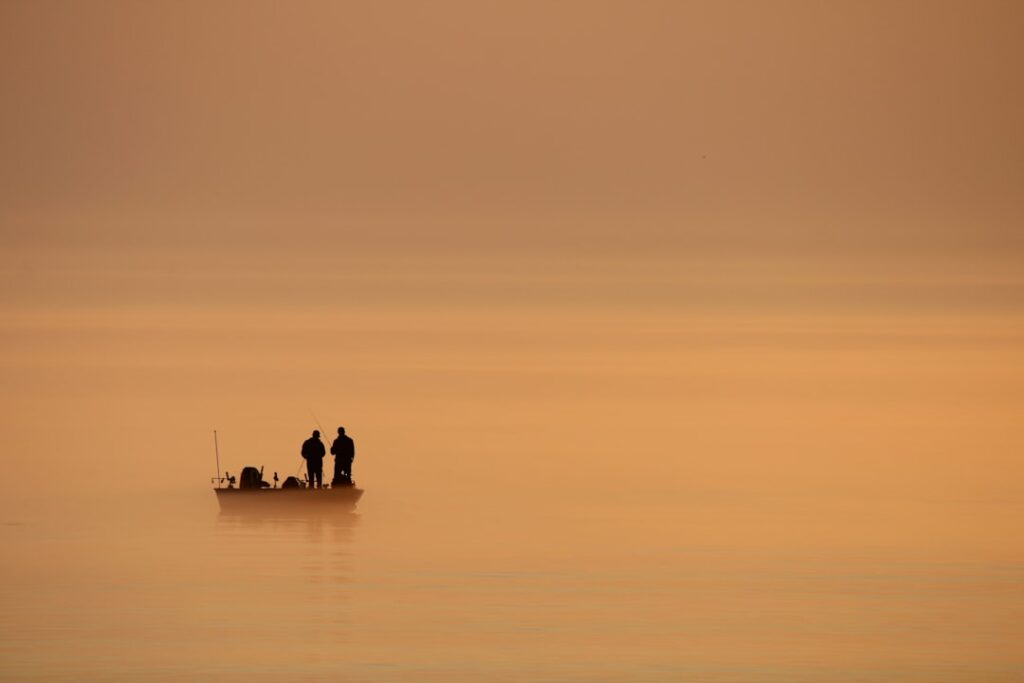 Two people fishing from a boat at sunrise.