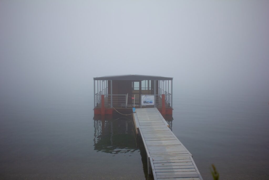 A dock with a small boat in the water on a foggy day